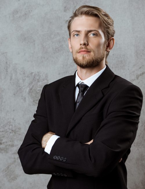 Young successful businessman posing with crossed arms over grey background. Copy space.